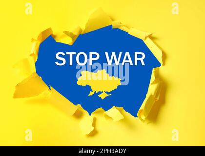 Stop war in Ukraine. Outline map of Ukraine and phrase on blue background, view through torn yellow paper Stock Photo