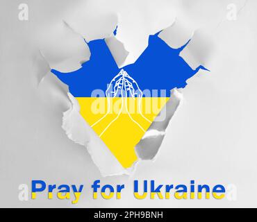 Pray For Ukraine. Ukrainian flag with illustration of hands, view through heart shaped hole in white paper with phrase Stock Photo