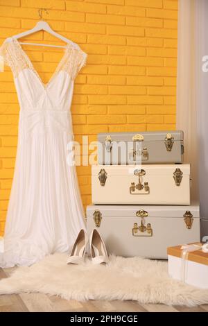 Storage trunks, gift box and beautiful wedding dress near yellow brick wall indoors. Interior design Stock Photo
