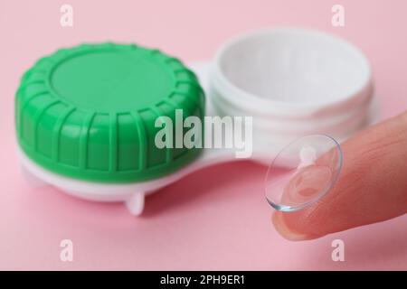 Woman with contact lens near case on pink background, closeup Stock Photo