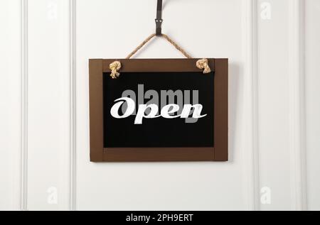 Small chalk board with word Open on white wall Stock Photo