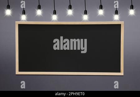 Glowing light bulbs and blackboard hanging on grey wall Stock Photo
