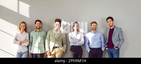 Successful smiling team of employees standing near gray wall Stock Photo