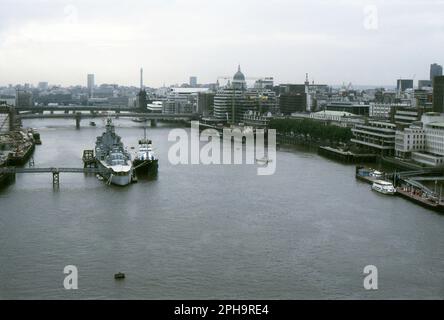 London. 1984. A view looking west from the upper footway of Tower Bridge, spanning the River Thames in London, England. Moored on the river is the Second World War period Royal Navy battlecruiser, H.M.S. Belfast, with another ship alongside. Beyond is London Bridge and Cannon Street railway bridge. On the north bank, The Northern & Shell Building, situated at 10 Lower Thames Street, is under construction. The Post Office Tower, St Paul’s Cathedral and The Monument are visible on the skyline. Stock Photo