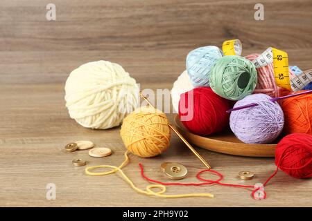 Clews of colorful knitting threads, crochet hooks, measuring tape and buttons on wooden table Stock Photo
