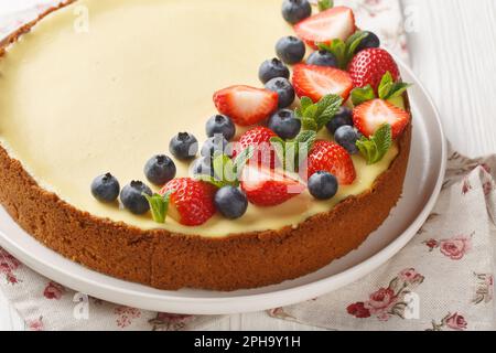 Whole round new york cheesecake with strawberries, blueberries and mint close-up on a plate on the table. Horizontal Stock Photo
