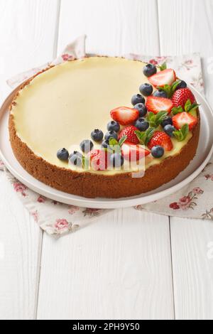 New York style classical cheese cake with fresh berries and mint closeup on the plate on the wooden table. Vertical Stock Photo