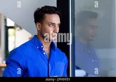 Thoughtful biracial man leaning on window and looking away Stock Photo