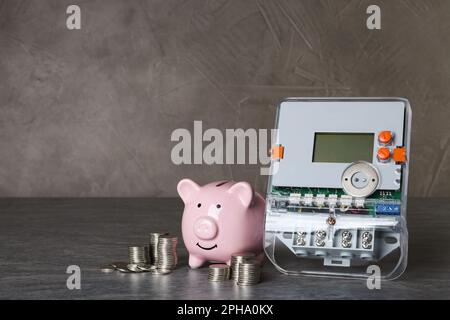 Electricity meter, piggy bank and coins on grey table. Space for text Stock Photo