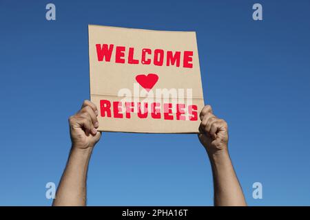 Man holding poster with phrase WELCOME REFUGEES outdoors, closeup Stock Photo