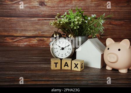 Tax alphabet letter with house model, piggy bank and alarm clock on wooden background Stock Photo