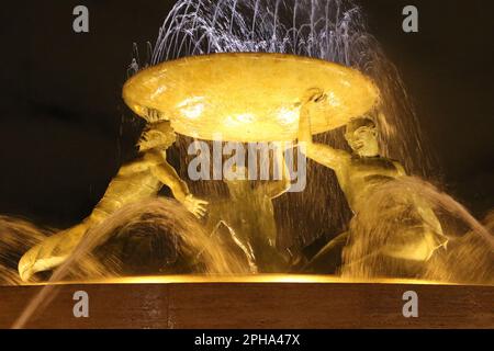 The Tritons’ Fountain (at night) is a fountain located just outside the City Gate of Valletta, Malta. It consists of three bronze Tritons holding up a large basin, balanced on a concentric base built out of concrete and clad in travertine slabs. The fountain is one of Malta's most important Modernist landmarks. Designed and constructed between 1952 and 1959. The bus terminal and station is located nearby. Stock Photo