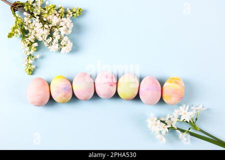 Happy Easter concept. Colorful Easter eggs with spring blooming daffodils and white lilac on a blue background. Stock Photo