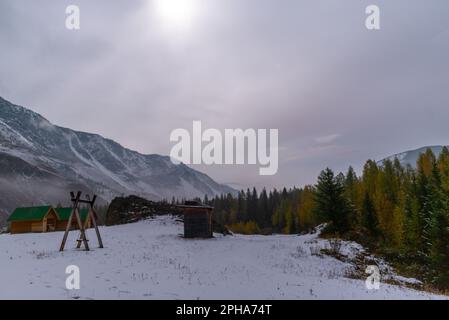 Swing at the holiday houses near the forest on the snow under the mountain with fog and white snow, with the light of the moon on a bright night in th Stock Photo