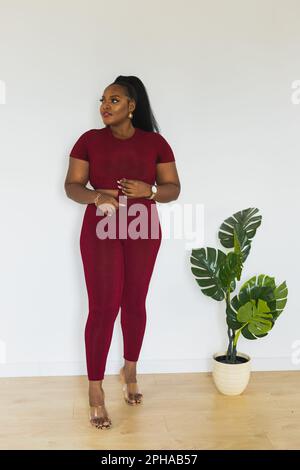 Premium Photo | Portrait of fat young african american woman standing  against white wall indoors female wearing a red short tshirt and leggings  sports home wear and inclusion with diversity concept