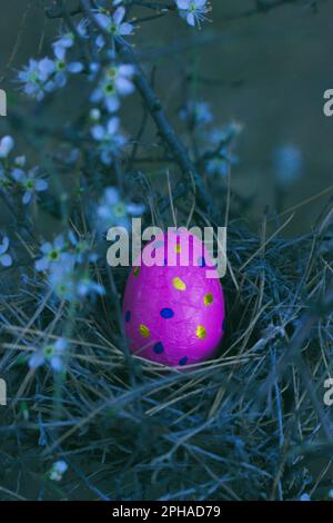 Pink sweet chocolate Easter egg in a bird's nest top view. Festive spring vertical background. Springtime holiday celebration. Easter still life with Stock Photo
