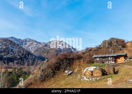A small rural house in the mountains with snow next to haystacks in Altai in autumn. Stock Photo