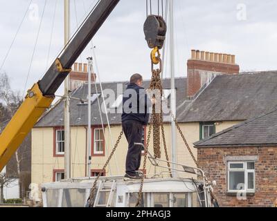 Man adjusts the chains prior to lowering a small boat in to the River Nith at Kingholm Quay, Scotland. Stock Photo