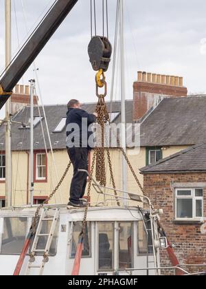 Man adjusts chains prior to lifting a small boat in to the River Nith, Kingholm Quay, Scotland. Stock Photo