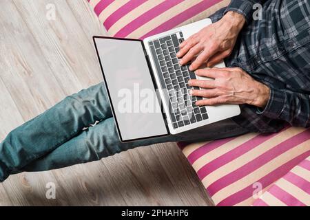 High angle view of man using a laptop with blank screen sitting on sofa. Stock Photo