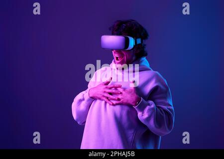 man in sweatshirt using virtual reality glasses on blue background. Neon lighting Stock Photo