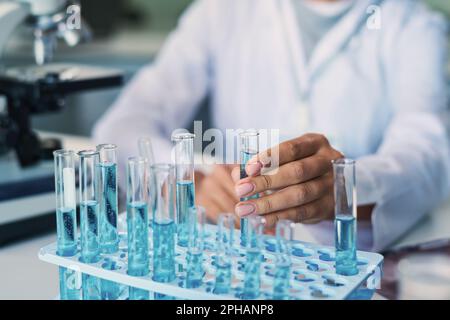 Hand of young female pharmacologist taking flask with sample of blue liquid substance before studying its characteristics in laboratory Stock Photo