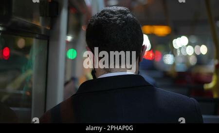 Back of male commuter riding bus at night after work. Passenger sitting inside public transportation Stock Photo