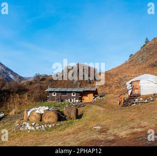 Haystacks and village house ail in mountains with snow in Altai in autumn. Stock Photo