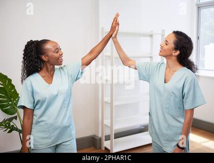 Two female doctors high five in clinic, wearing scrubs celebrate success Stock Photo