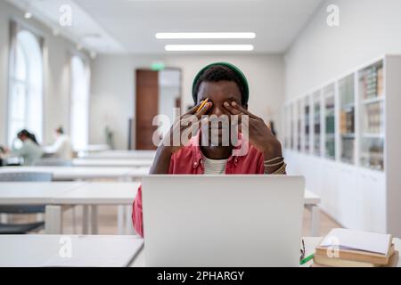 Tired African guy university student sitting in library feeling exhausted after online classes Stock Photo
