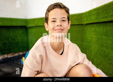 Portrait of attractive happy smiling 11 years old boy, outdoor over green wall. Happy handsome teenager. Cute kid's portrait. Stock Photo