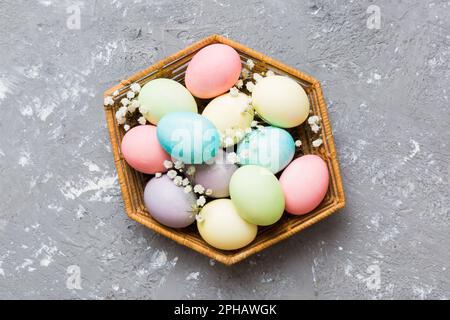 Happy Easter composition. Easter eggs in basket on colored table with gypsophila. Natural dyed colorful eggs background top view with copy space. Stock Photo