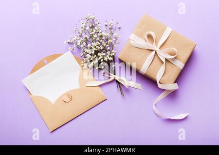 Wedding mockup with white paper list and flowers gypsophila on colored table top view flat lay. Blank greeting cards and envelopes. Beautiful floral p Stock Photo