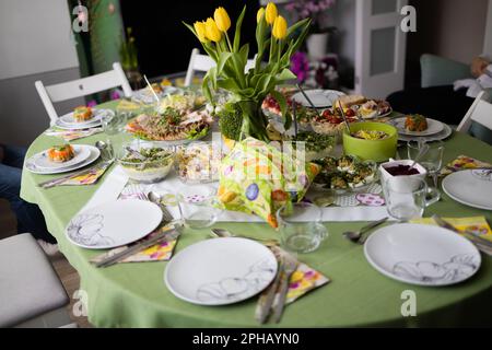 Traditional Easter dishes with white borscht, sausage, eggs, salad and cakes on festive table in Poland. Home interior with easter decor. Spring Stock Photo