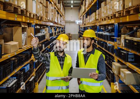 Warehouse workers checking stuff in warehouse with digital system in tablet. Stock Photo