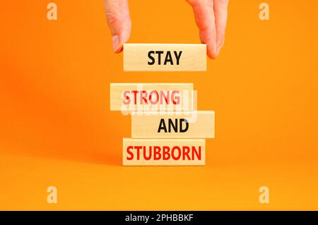 Stay strong and stubborn symbol. Concept words Stay strong and stubborn on wooden block. Beautiful orange table orange background. Motivational busine Stock Photo