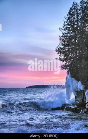 Frigid surf pounds the icy Lake Superior shoreline under a sunset sky painted in vivid pink and magenta hues Stock Photo