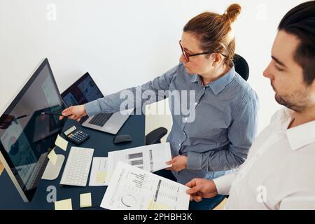 Businesswoman discussing financial data with her colleague standing at desk in office. Woman entrepreneur working with charts and tables on computer. Stock Photo