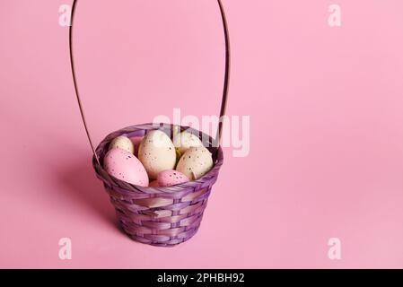 Purple wicker basket filled with multi-colored Easter eggs in pastel colors on a pink background. Copy advertising space Stock Photo