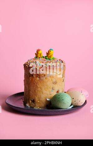 Still life with Easter cake and colorful eggs on navy ceramic plate, isolated over pink background. Vertical studio shot Stock Photo