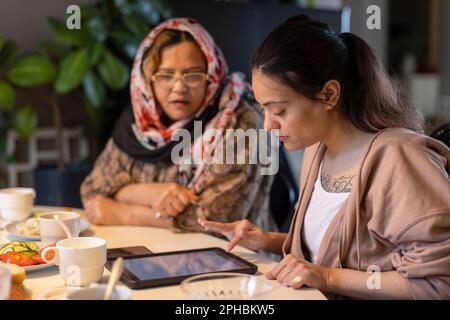 Young woman with paraplegia using tablet PC by mother sitting at dining table Stock Photo