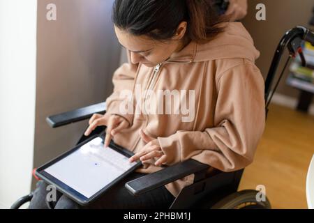 High angle view of woman with paraplegia using tablet PC while sitting on wheelchair at home Stock Photo