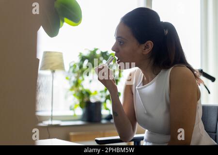 Young woman with paraplegia applying lipstick at home Stock Photo