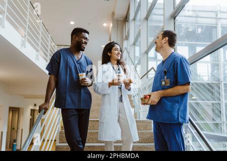 Happy multiracial healthcare workers talking while standing on staircase at hospital Stock Photo