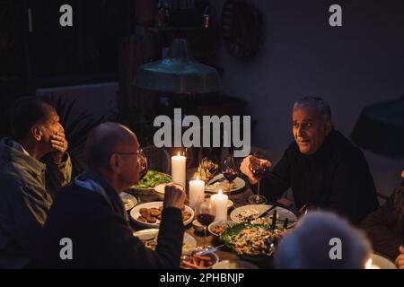 Male friends talking to each other during dinner party at night Stock Photo