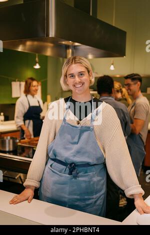 Portrait of smiling non-binary student wearing apron while standing in kitchen during cooking class Stock Photo