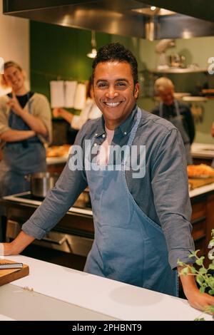 Portrait of happy mature male student standing in kitchen during cooking class Stock Photo