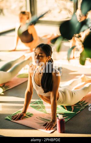 Young woman doing cobra stretch on exercise mat during yoga class at retreat center Stock Photo