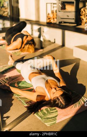 Young woman stretching while lying on exercise mat at retreat center Stock Photo