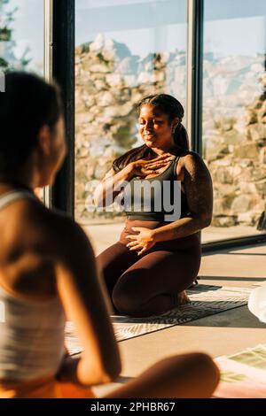 Smiling woman practicing breathing exercise in yoga class at retreat center Stock Photo